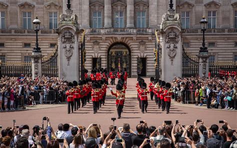 Tematica: Il celebre cambio della guardia a Buckingham Palace con le giubbe rosse e gli alti cappelli neri, in presenza di turisti.