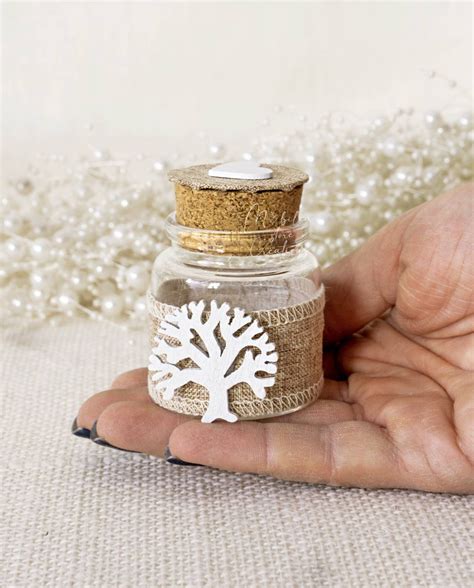 Barattolino in vetro trasparente con tappo in sughero, decorato con ciondolo a forma di Albero della Vita e fiocco, pronto per contenere confetti.
