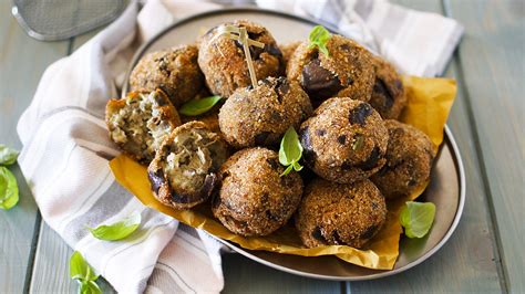 Tavola con polpette di melanzane e basilico, accompagnate da foglie di basilico fresco
