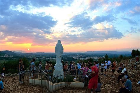 Descrizione: Immagine di pellegrini che salgono la collina del Podbrdo a Medjugorje, con la statua della Madonna in cima.