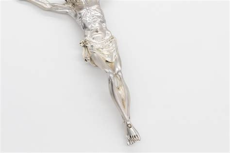 Dettaglio ravvicinato della figura di Cristo in argento su un crocifisso in legno d'ulivo, evidenziando l'espressione sofferente e i dettagli anatomici
