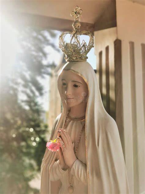 Un'immagine ravvicinata di una statua della Madonna di Fatima con corona dorata e mani giunte, con uno sfondo sfocato di un santuario