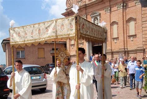 Una processione del Corpus Domini con fedeli che seguono il sacerdote con l'ostensorio sotto un baldacchino.