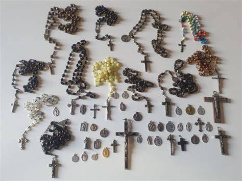 Foto d'insieme che mostra vari oggetti religiosi, tra cui crocifissi, rosari e portachiavi spirituali su una superficie naturale.