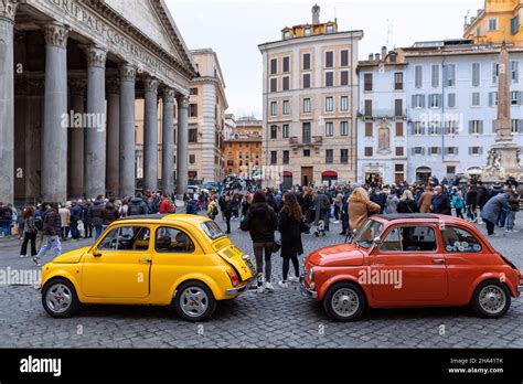 Foto di diverse Fiat 500 d'epoca parcheggiate in una piazza, con persone che le ammirano.
