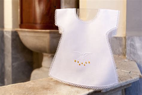 Una candela battesimale accesa accanto a una veste bianca, simboli di fede e nuova nascita.