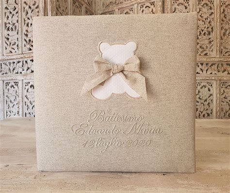 Album battesimo con copertina in tessuto di cotone naturale, decorato con dettagli argentati.