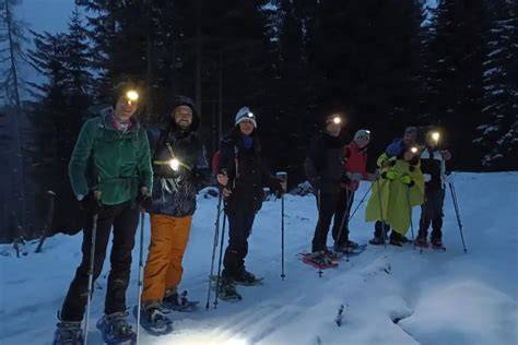 Escursionisti con ciaspole in un bosco innevato delle Dolomiti al tramonto
