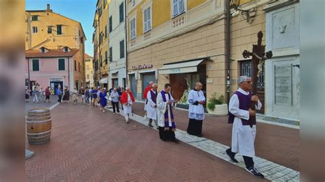 Sacerdote che guida una processione in un piccolo paese, con la comunità che lo segue