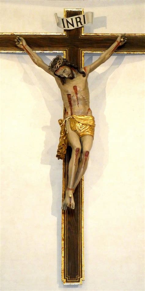 Dettaglio di un crocifisso moderno con figura di Cristo in alluminio lucido e croce in legno scuro.