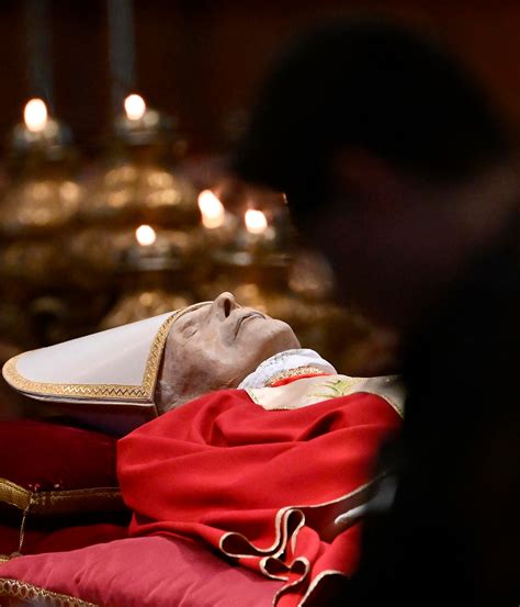Foto della salma di Papa Benedetto XVI esposta nella Basilica di San Pietro con fedeli in fila per l'omaggio.