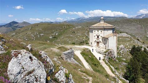 Veduta panoramica della chiesa di Santa Maria della Pietà situata nel paesaggio montano dell'Abruzzo con il castello di Rocca Calascio sullo sfondo.