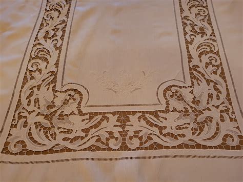 Dettaglio fotografico di un ricamo a punto Richelieu su tovaglia d'altare con motivi floreali e simboli religiosi