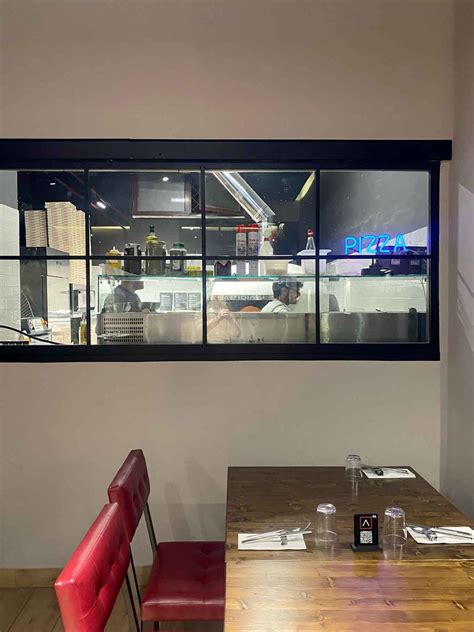 Interno della Pizzeria Gli Artigiani con stile industrial-minimalista, sedute rosse e tavoli in legno