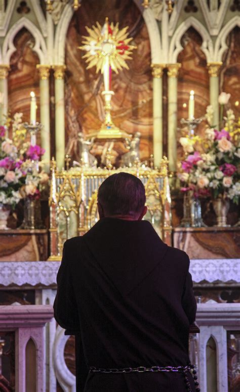 un sacerdote in adorazione davanti al Santissimo Sacramento esposto, con fedeli in ginocchio