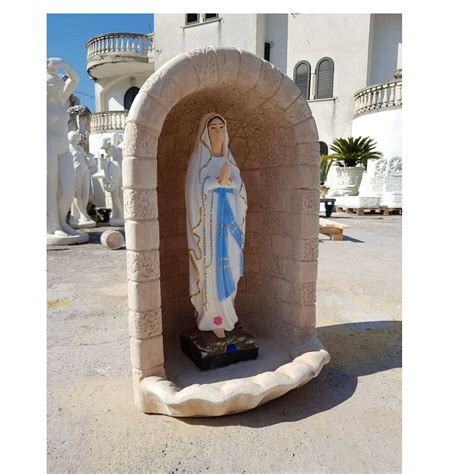 Foto di una statua della Madonna posizionata all'interno di una grotta o nicchia in un giardino