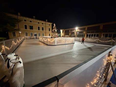 Dettaglio della pista di pattinaggio su ghiaccio con persone di diverse età che pattinano e segnaletica informativa
