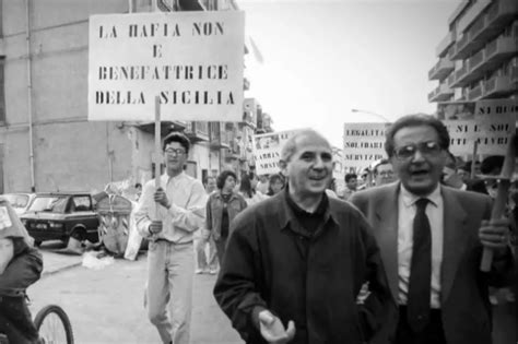 Ritratto di Don Pino Puglisi con un sorriso, magari con sfondo il quartiere di Brancaccio
