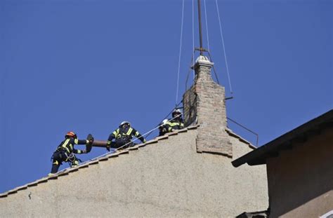 Un'inquadratura suggestiva del comignolo della Cappella Sistina stagliato contro il cielo di Roma, con una folla di fedeli in attesa in Piazza San Pietro