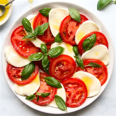 Foto di insalata Caprese classica su un piatto da portata, con fette di pomodoro e mozzarella alternate e foglie di basilico fresco