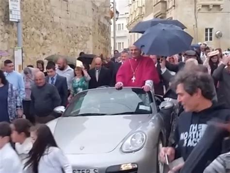 sacerdote Gwann Sultana in piedi su una Porsche argentata trainata da bambini durante una processione
