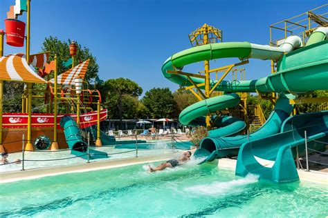 Bambini che giocano e si divertono in un parco acquatico con scivoli e piscine, sotto il sole estivo. Foto tematica CRE.