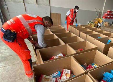 Volontari Caritas che preparano o distribuiscono pacchi alimentari, con alimenti non deperibili in evidenza