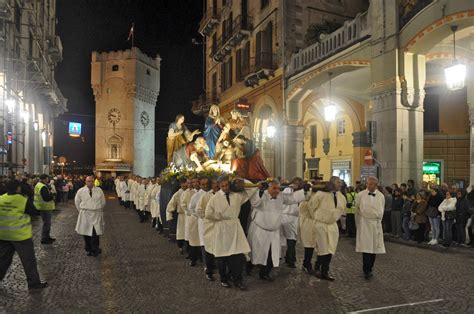 Foto di una processione religiosa con fedeli che portano statue e stendardi, in una strada cittadina