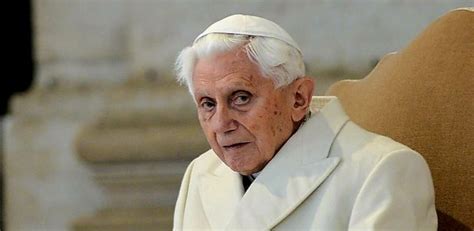 Foto di Papa Emerito Benedetto XVI in età avanzata, magari mentre legge o prega con un deambulatore vicino.