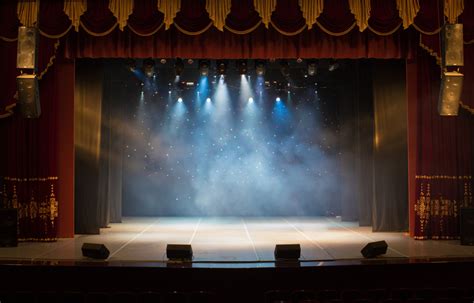 Interno di un teatro con luci soffuse, focus sul palco vuoto e sedie vuote, per trasmettere un senso di esclusività e preparazione.