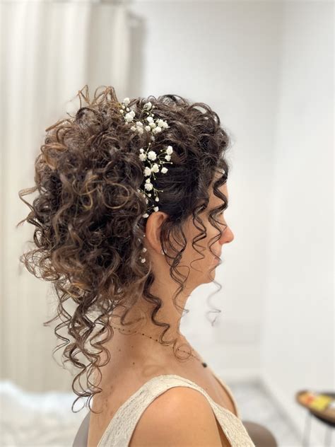 Sposa con capelli ricci lunghi raccolti in un semiraccolto basso impreziosito da fiori e perle.